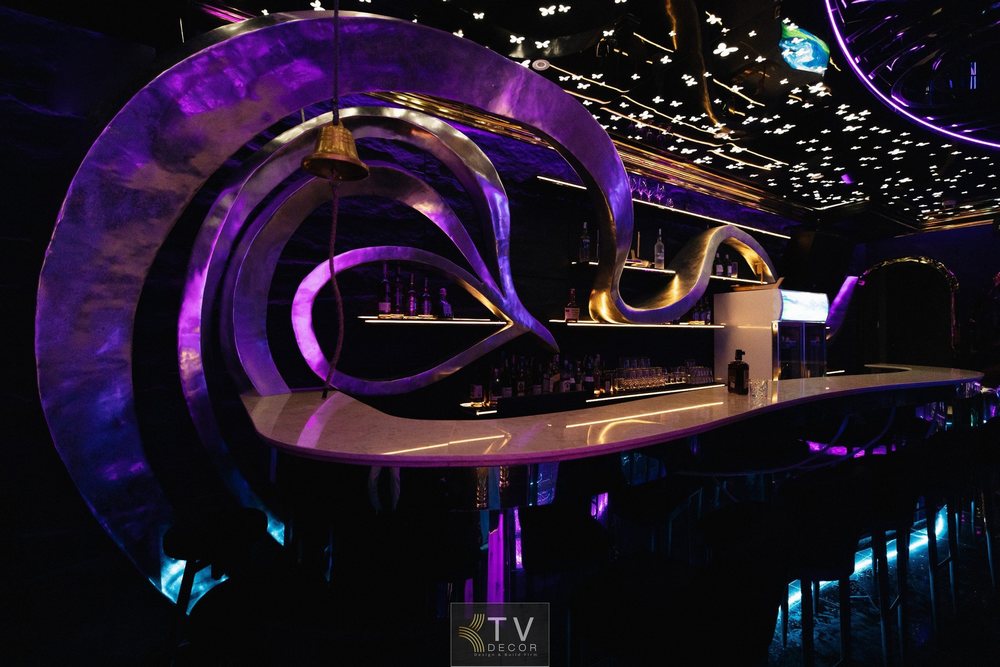 Không gian Lounge 100m² được KTV DECOR tối ưu bằng thiết kế quầy bar nghệ thuật với khung uốn lượn kim loại, ánh sáng tím kết hợp trần LED hình cánh bướm. Lý tưởng cho mô hình nightlife hiện đại, đậm dấu ấn thương hiệu.