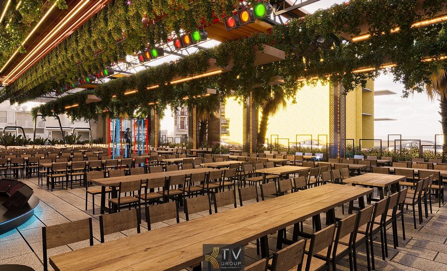 Không gian Beer Garden rộng thoáng với dãy bàn gỗ dài, trần phủ cây xanh và hệ thống đèn LED nhiều màu tạo cảm giác sôi động. Khu sân khấu và ánh sáng trang trí nổi bật mang lại không khí giải trí hiện đại.