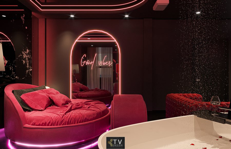 Bàn nhỏ cạnh bồn tắm với ly rượu vang tạo bầu không khí lãng mạn cho các cặp đôi.  Tường tối màu giúp làm nổi bật ánh sáng neon và nội thất đỏ của căn phòng.