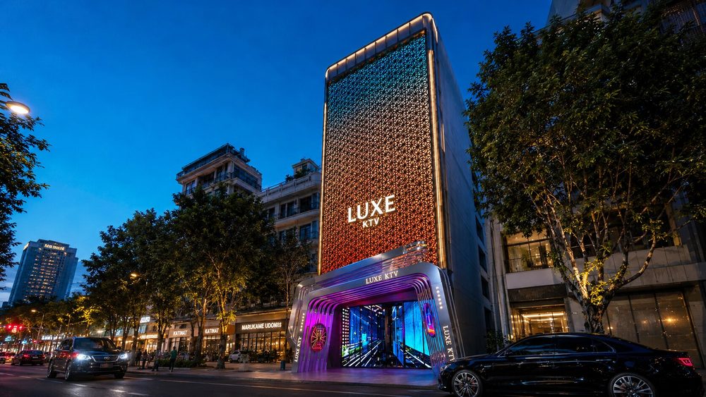 Mặt tiền LUXE KTV cao tầng hiện đại với facade họa tiết độc đáo, đèn LED chuyển màu và sảnh karaoke sang trọng.